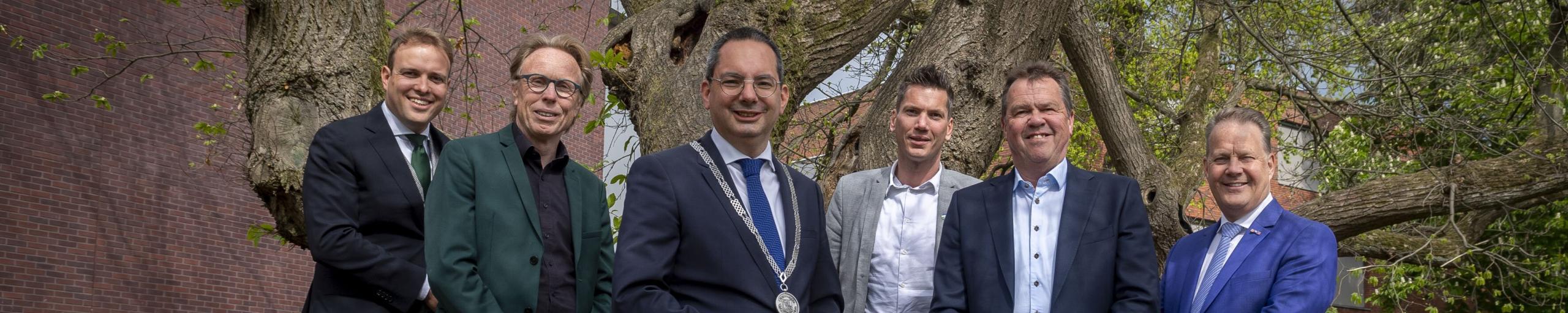 Foto van het college van burgemeester, wethouders en waarnemend gemeentesecretaris. Van links naar rechts: Wethouder de Heer, Wethouder van der Beek, Burgemeester Adriaansen, Wethouder van Agtmaal, Wethouder Schuurbiers, waarnemend gemeentesecretaris Bogers